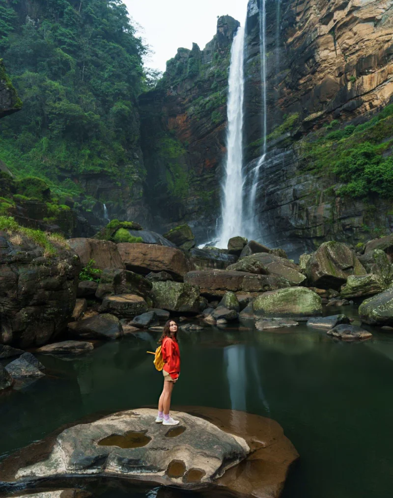 traveler-standing-on-rocks-beside-a-tall-waterfall-in-sri-lankas-hill-country