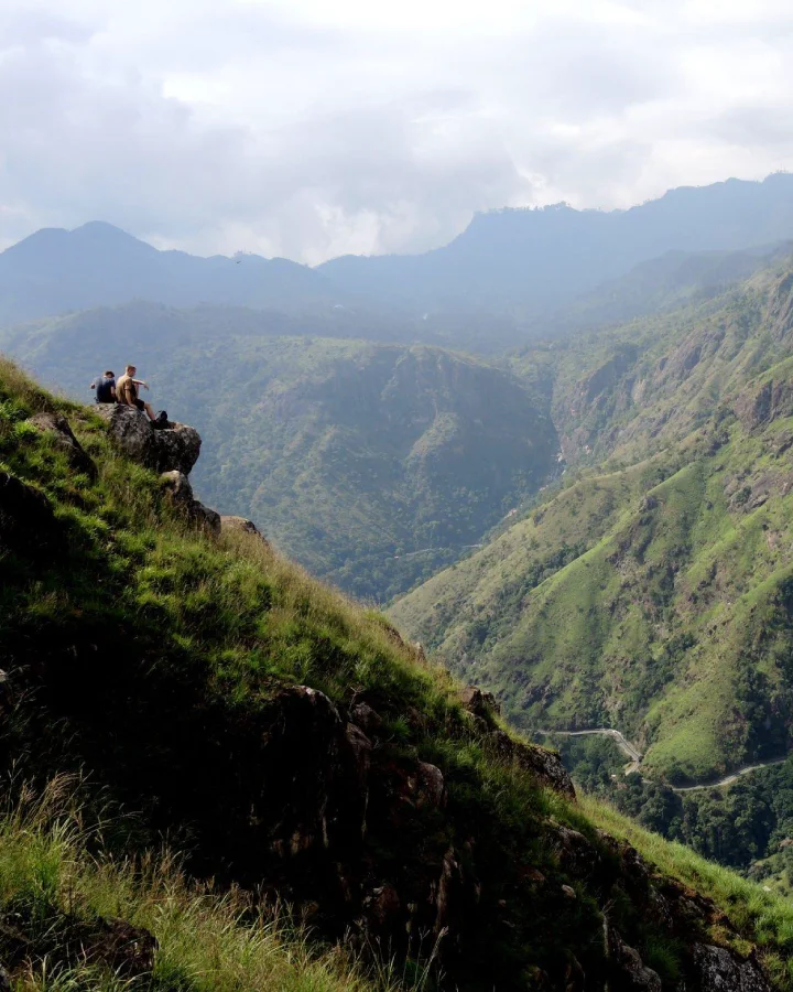 Hikers resting on a cliff overlooking the green valleys and mountains of Ella Rock