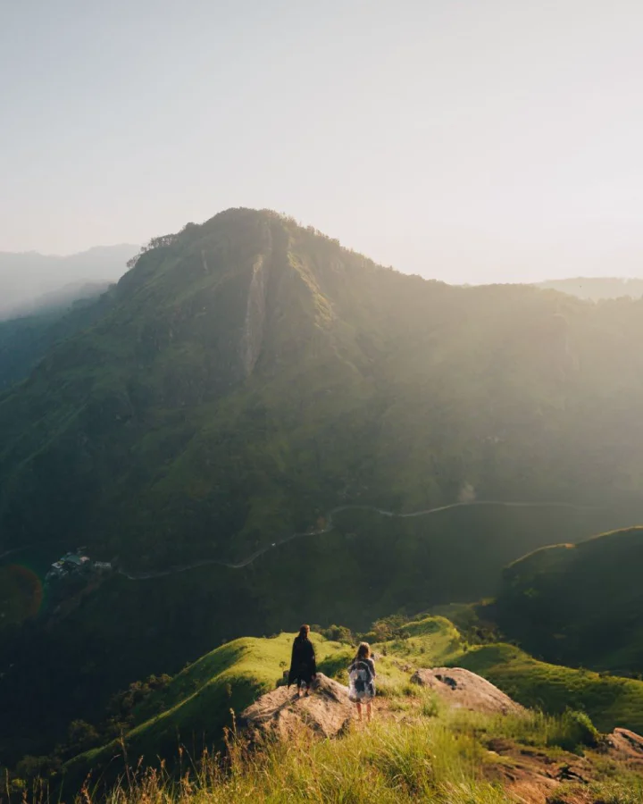 Two people standing on a hilltop at Little Adam’s Peak, overlooking green